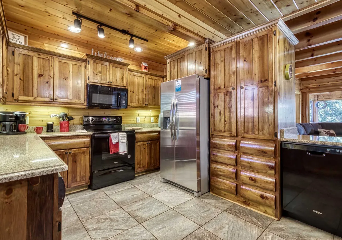 A warm, homely kitchen featuring wooden cabinetry, stainless steel appliances, and elegant granite countertops. The space is well-lit and designed for cooking, meal preparation, and gathering with friends or family.