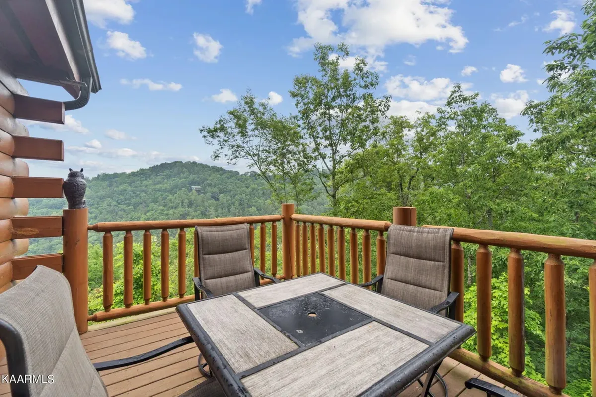 A wooden deck with comfortable outdoor seating, offering sweeping views of the Smoky Mountains under a clear sky. The deck extends the living area outdoors, providing an ideal space for socializing or quiet reflection amid natural beauty.