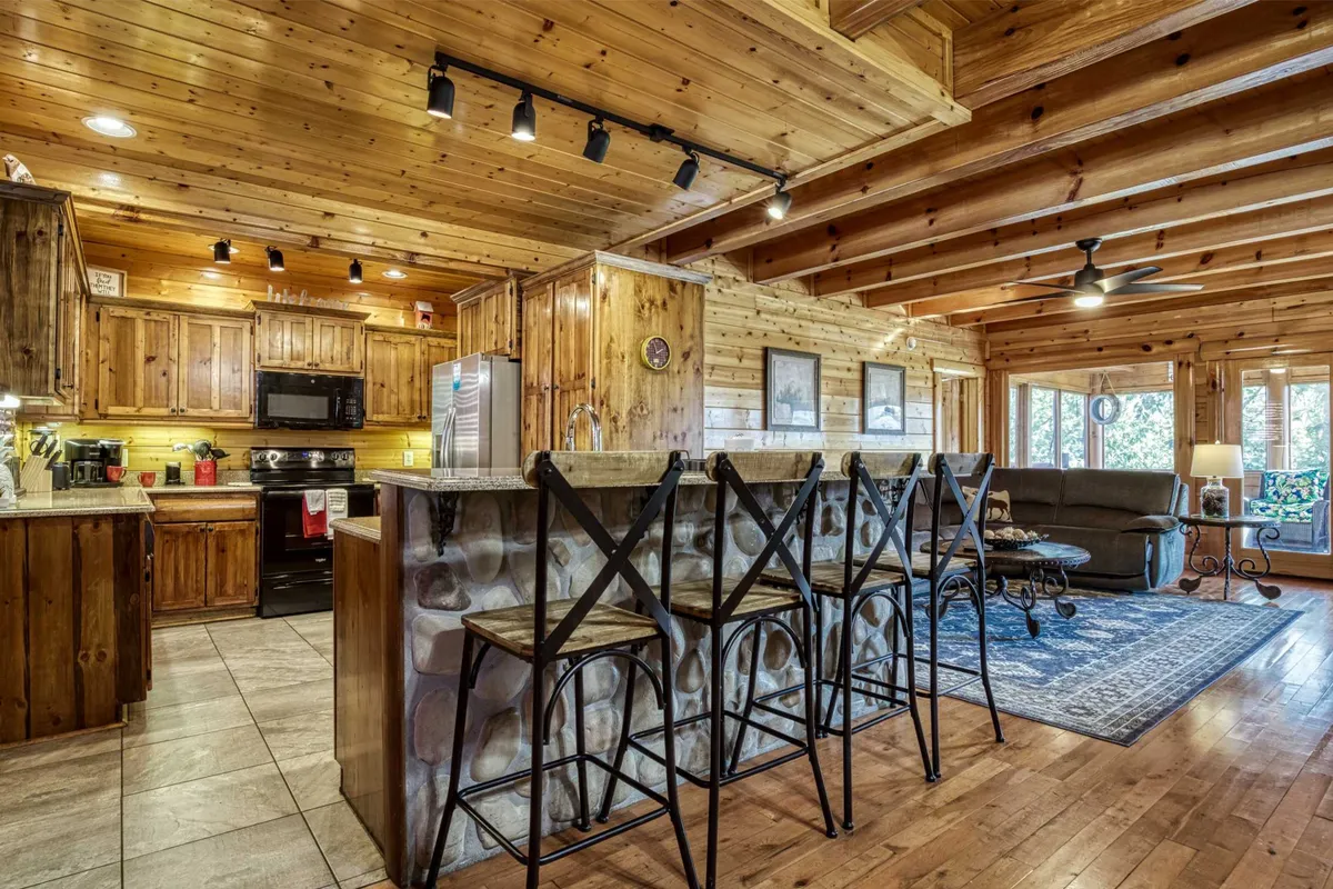A welcoming open-concept kitchen and dining space with wooden cabinetry, a kitchen island with bar stools, a comfortable sofa, and large windows that let in natural light. The layout is ideal for both cooking and casual gatherings.