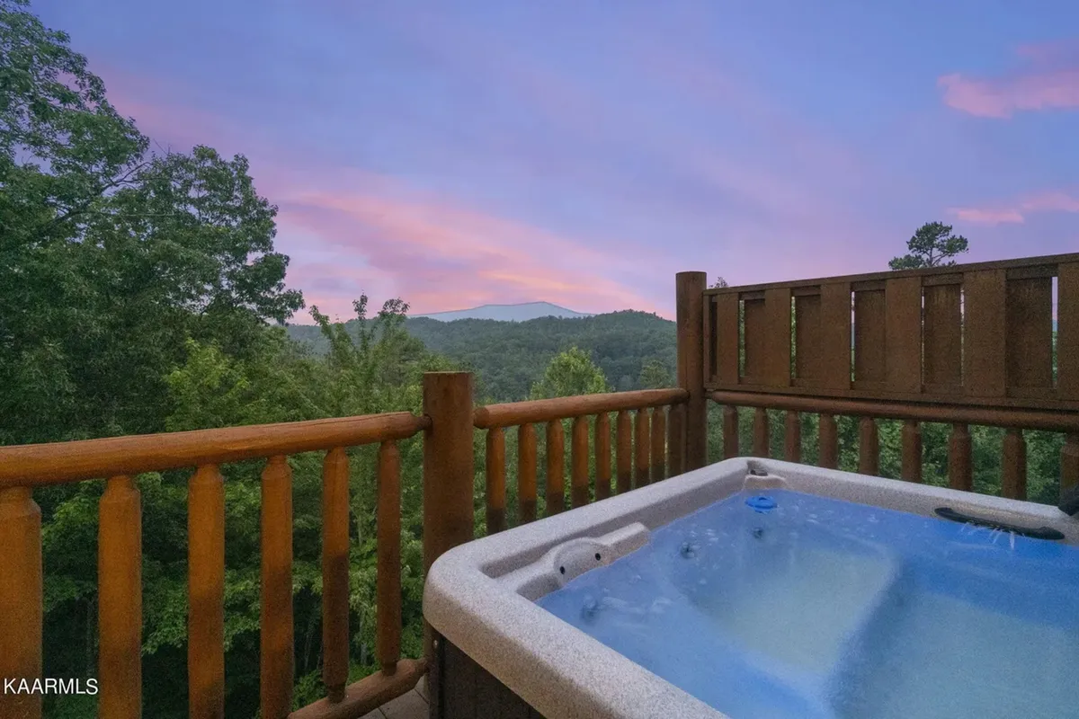 A steaming hot tub sits on a wooden deck overlooking a stunning mountain vista bathed in sunset light. The scene feels inviting and restful, suggesting a perfect way to unwind after a day of hiking or exploring the great outdoors.