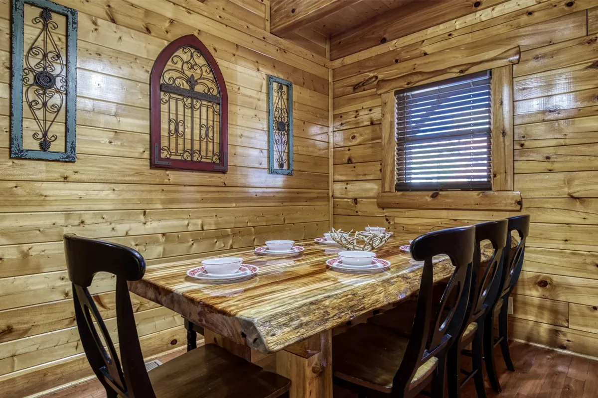 A warm, inviting dining room with a solid wooden dining table, decorative wall art, and a window with blinds allowing natural light to stream in. The setup is perfect for family meals and intimate gatherings.