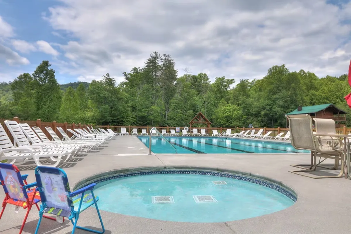 This image captures a sparkling swimming pool surrounded by a hot tub, lounge chairs, and lush greenery. The setting is bright and inviting, with space for sunbathing, socializing, and relaxing poolside. The pool is clearly a shared amenity, offering a communal space for guests to gather and enjoy resort-style leisure.