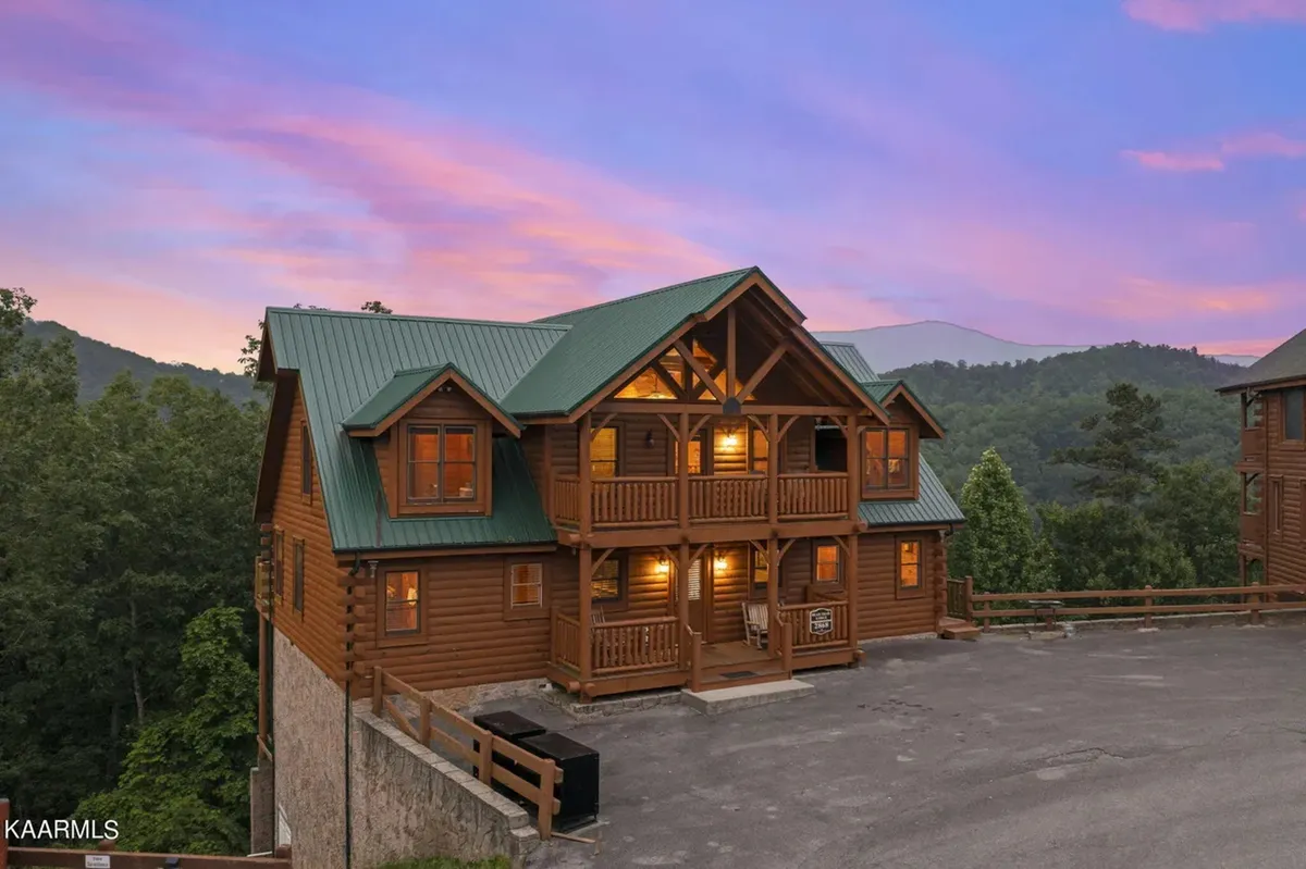 This image showcases a classic log cabin with a green metal roof, wood balconies, and the surrounding mountains under a warm sunset sky. The inviting porch and wooden railings are perfect for group barbecues and evening relaxation, reflecting a sense of peace and togetherness in an exclusive mountain community.