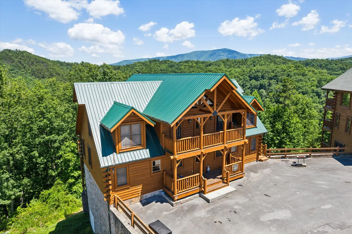A welcoming log cabin exterior with a green metal roof and scenic mountain backdrop. The balcony and surrounding landscape invite residents and guests to enjoy the outdoors, whether for nature walks, stargazing, or simply relaxing in the fresh mountain air.
