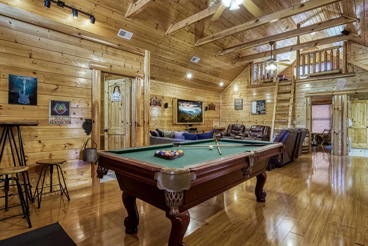 A game room with a pool table at its center, exposed wooden beams, comfortable seating, and wall art. The design fosters a fun, relaxed vibe—ideal for friendly competitions and family game nights.