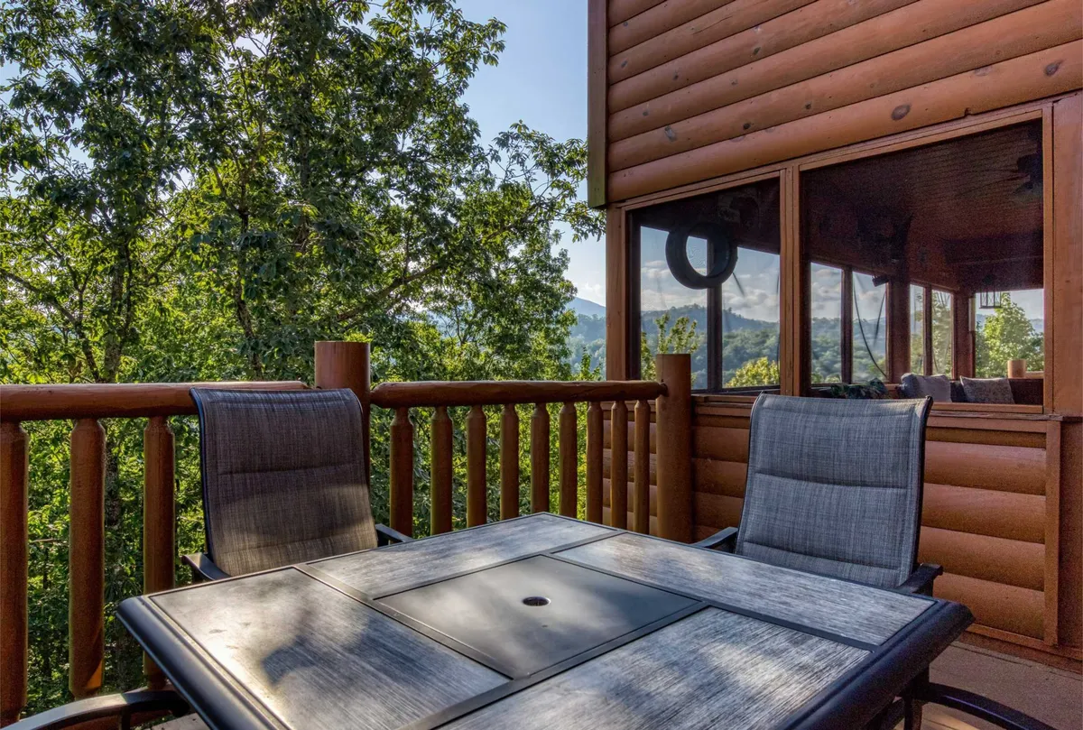 The image presents a serene outdoor dining area on a deck, featuring a wooden table and chairs with panoramic mountain vistas in the background. The setting is ideal for sharing a sunrise breakfast, sunset dinner, or a quiet moment with coffee as described in the section.